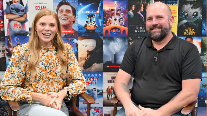 Two people sitting in front of a backdrop with movie covers on it